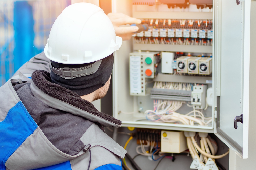 Electrician in a winter coat checking an electrical panel 